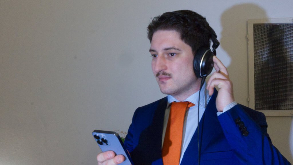 Patrick Pehl mit orangefarbener Krawatte mit iPhone und Kopfhörern - 19-9
