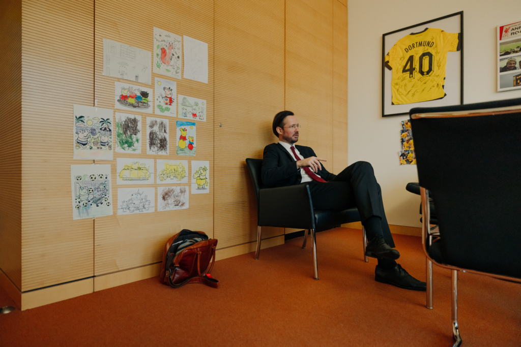 SPD Vize und Seeheimer Sprecher Dirk Wiese (MdB) sitzt in einem Konferenzsessel, im Hintergrund Ausmalbilder von seinem Kind und ein Tricot des FC Dortmund.