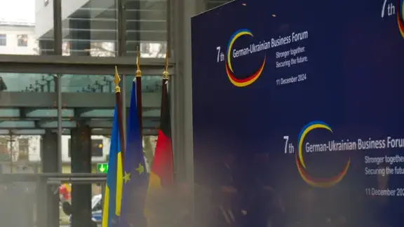 header-mobil (576x324 px) 7. Deutsch-Ukrainisches-Wirtschaftsforum in Berlin am 11. Dezember 2024 - abgebildet sind drei Falggen (Deutschland EU, Ukraine) vor einer Stellwand