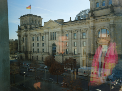 Der Reichstag aus dem Paul-Löbe-Haus heraus mit einer Person, die einen Berliner-Ensemble-Fanschal in der Spiegelung einer Fensterscheibe