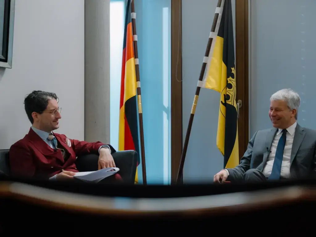 Parlamentarischer Geschäftsführer des CDU/CSU-Fraktion im Bundestag Steffen Bilger (CDU) im Gespräch mit Patrick Pehl im Jakob-Kaiser-Haus. Im Hintergrund eine Bundesflagge und eine Fahne des Landes Baden-Württemberg