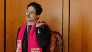 Patrick Pehl mit Fanschal des Berliner Ensemble und einer Aktentasche bei einem Interview im Bundestag